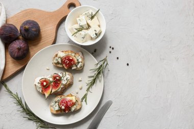 Beyaz zemin üzerinde ricotta ve mavi peynirli lezzetli incirli bruschetta tabağı.