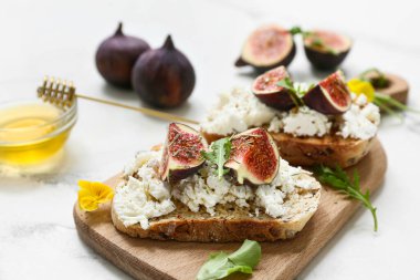 Beyaz arka planda ricotta peyniri ve roka ile lezzetli incir bruschetta tahtası, yakın plan.