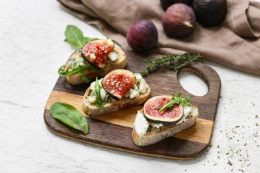 Beyaz arka planda farklı peynirler ve roka ile lezzetli incirli bruschetta tahtası.