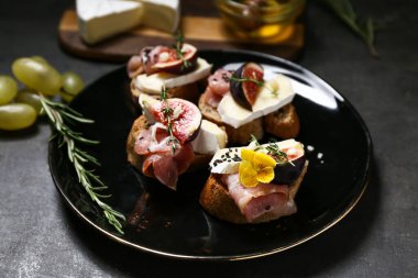 Bir tabak lezzetli incirli bruschetta Prosciutto ve siyah arkaplanda Camembert peyniri.