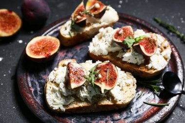 Siyah arka planda ricotta peynirli lezzetli incirli bruschetta tabağı, yakın plan.
