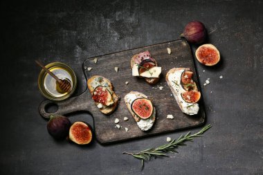 Farklı peynirler ve siyah arka planda bir kase bal ile lezzetli incirli bruschetta tahtası.