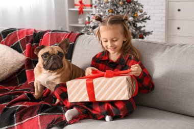 Fransız bulldog 'u ve Noel hediyesi olan sevimli küçük kız evdeki kanepede oturuyor.