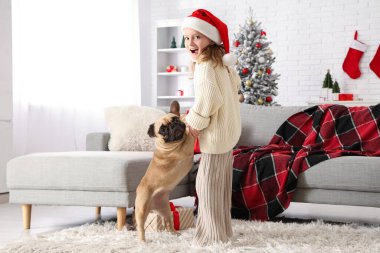 Evde buldogla oynayan Noel şapkalı sevimli küçük kız.