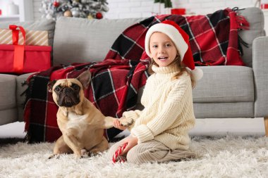 Evde buldogla oynayan Noel şapkalı sevimli küçük kız.