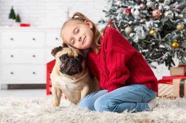 Sıcak kıyafetler içinde sevimli küçük bir kız evde Fransız bulldog 'una sarılıyor.
