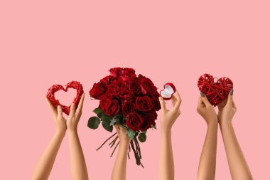 Gülleri, kalpleri ve pembe arka planda nişan yüzüğü olan kadın elleri. Sevgililer Günü kutlaması