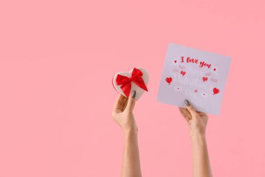 Hediye kutusu ve pembe arka planda tebrik kartı olan kadın elleri. Sevgililer Günü kutlaması