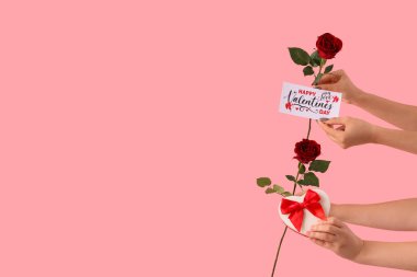 Güllü kadın elleri, hediye kutusu ve pembe arka planda tebrik kartı. Sevgililer Günü kutlaması