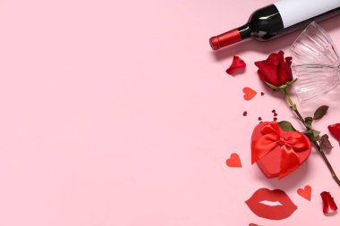 Hediye kutulu güzel kırmızı gül, kağıt kalpler ve pembe arka planda bir şişe şarap. Sevgililer Günü kutlaması