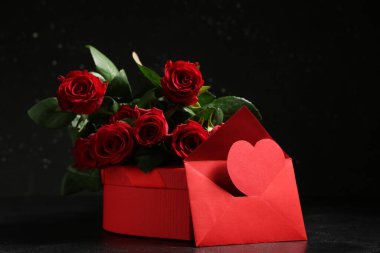Zarflı güzel kırmızı güller ve siyah arka planda hediye kutusu. Sevgililer Günü kutlaması