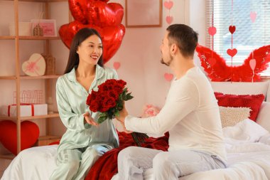 Sevgililer Günü 'nde yatak odasında kocasından gül alan genç bir Asyalı kadın.