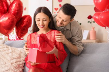 Sevgililer Günü 'nde eşiyle birlikte evde hediye kutusu açan genç bir adam.