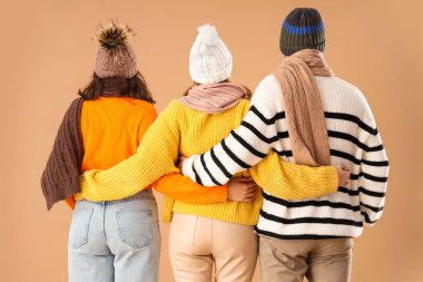 Sonbahar kıyafetleri içinde bej arka planda sarılan erkek ve iki güzel kadın. Poliyamory konsepti