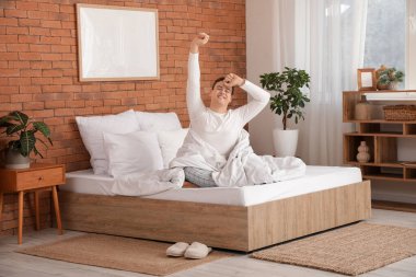 Uykulu genç adam evde yatakta geriniyor.