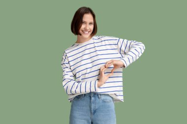 Güzel genç bir kadın yeşil arka planda elleriyle kalp yapıyor.