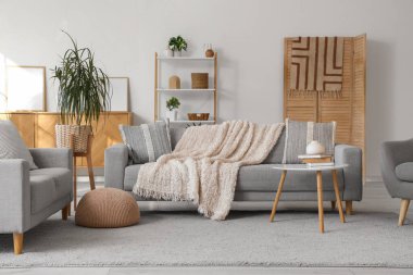 Gri koltukları, raf ünitesi ve katlanır ekranı olan oturma odasının içi.