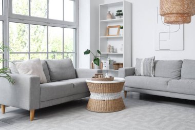 Gri koltukları, raf ünitesi ve masası olan aydınlık oturma odasının içinde.