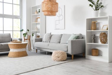 Gri koltukları, raf üniteleri ve masası olan aydınlık oturma odasının içinde.