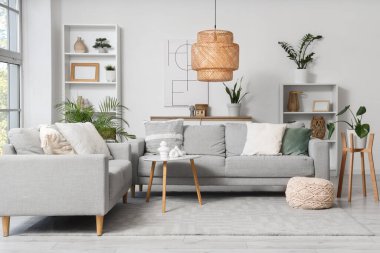 Gri kanepeler, raf üniteleri ve bitkilerle aydınlık oturma odasının içinde.