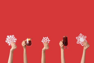 Süslü kar taneleri, cam ve bir kupa lezzetli sıcak şaraplı kırmızı arka planda kadın elleri.