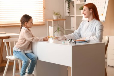 Kadın göz doktoru klinikteki küçük kıza gözlük veriyor.