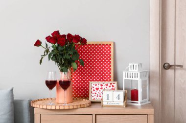 Sevgililer Günü kutlamaları için dekore edilmiş oturma odasının içi aydınlık duvarın yanındaki çekmecelerde şarap ve gül çiçekleriyle süslenmiş.