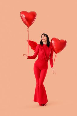 Aşk tanrısı gibi giyinmiş, bej arka planda kalp şeklinde balonları olan güzel, genç ve mutlu bir kadın. Sevgililer Günü kutlaması