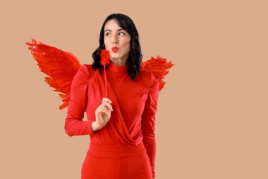 Tüylü aşk tanrısı gibi giyinmiş güzel, genç bir kadın bej arka planda öpücük yolluyor. Sevgililer Günü kutlaması