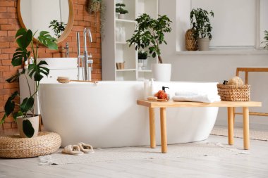 Küvetli, çiçekli ve ahşap banklı şık bir banyo.