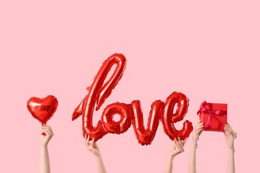 Balon şekilli kadın elleri. Aşk kelimesi şeklinde balon, kalp şeklinde balon ve pembe arka planda hediye kutusu. Sevgililer Günü kutlaması