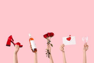 Zarf tutan kadın eller, cam, yüksek topuklu ayakkabı, şarap şişesi ve pembe arka planda kırmızı güller. Sevgililer Günü kutlaması