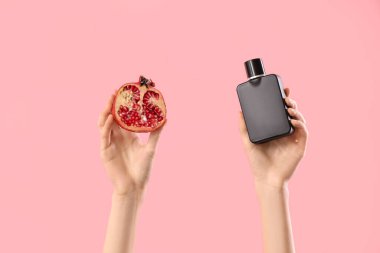 Pembe arka planda parfüm ve nar şişesi olan kadın elleri.