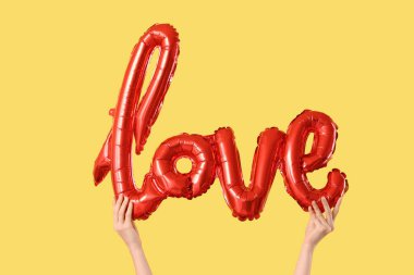 Sarı arka planda aşk kelimesi şeklinde balonu olan kadın eller. Sevgililer Günü kutlaması