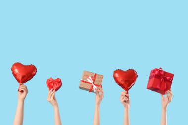 Kalp şeklinde balonları ve mavi arka planda hediye kutuları olan kadın elleri. Sevgililer Günü kutlaması