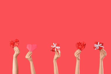 Hediye kutularıyla kadın elleri ve kırmızı arka planda kağıt kalp. Sevgililer Günü kutlaması