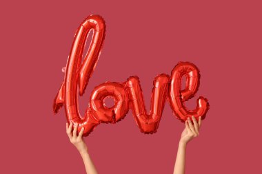 Kırmızı arka planda aşk kelimesi şeklinde balonu olan kadın eller. Sevgililer Günü kutlaması