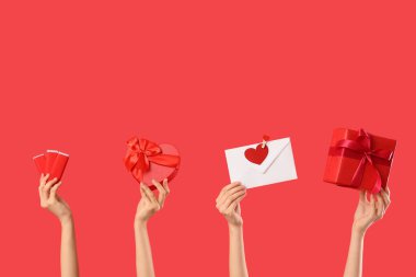 Hediye kutuları, çikolata çubukları ve kırmızı arka planda zarf olan kadın elleri. Sevgililer Günü kutlaması