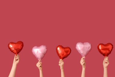 Kırmızı arka planda kalp şeklinde balonları olan kadın elleri. Sevgililer Günü kutlaması