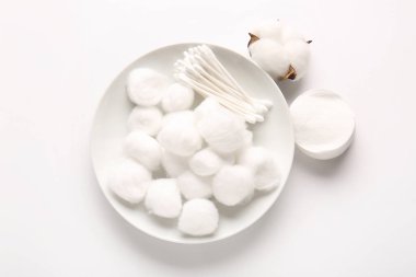 Beyaz arka planda pamuk topları, bezler, pedler ve çiçeklerle kaplı bir tabak.
