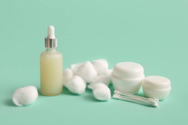 Cotton balls with swabs, bottle of cosmetic oil and jars of cream on turquoise background clipart