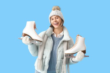 Mavi arka planda buz patenleriyle kışın giyinmiş genç bir kadın.