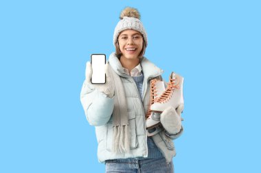 Kışın buz pateni ve mavi arka planda cep telefonu olan genç bir kadın.