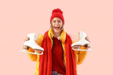 Pembe arka planda buz patenleriyle kışın giyinmiş mutlu genç bir kadın.