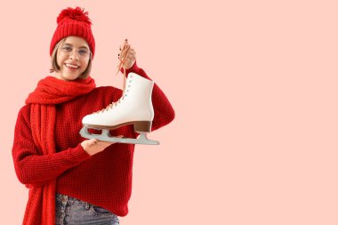 Pembe arka planda buz pateni yapan kışlık elbiseli genç bir kadın.