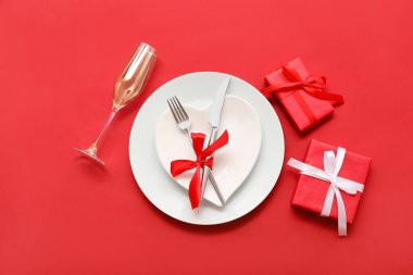 Kırmızı arkaplanda hediye kutuları ve ipek kurdeleyle Sevgililer Günü için masa ayarı