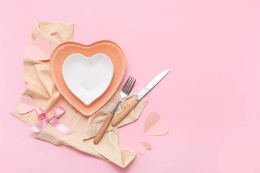 Kalp şeklinde tabaklar, kurdele, peçete ve pembe arka planda kağıt kalplerle Sevgililer Günü için masa ayarı