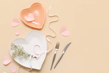 Bej arkaplanda kalp şeklinde tabaklar, çiçekler, kurdele ve kağıt kalplerle Sevgililer Günü için masa ayarı