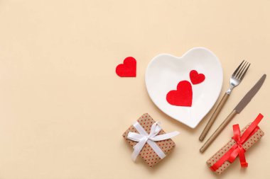 Kalp şeklinde tabaklar, hediye kutuları ve bej arka planda kağıt kalplerle Sevgililer Günü için masa ayarı