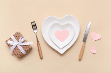 Kalp şeklinde tabaklar, hediye kutusu ve bej arka planda kağıt kalplerle Sevgililer Günü için masa ayarı